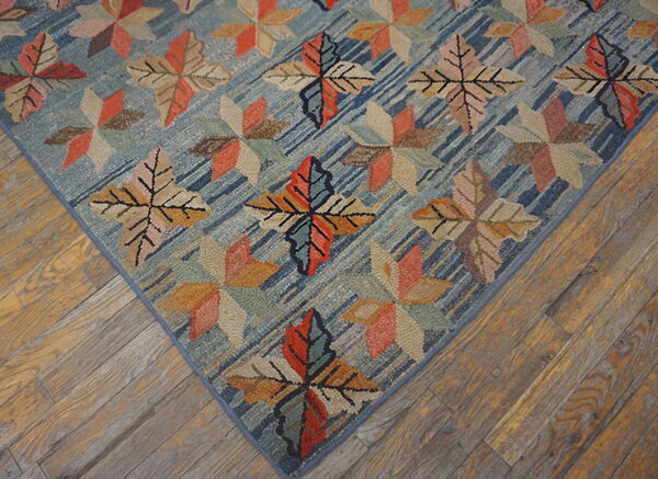 Multicolored leaf and geometric patterns cover a textured blue rug resting on rustic wood flooring.