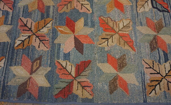 Blue hooked rug featuring large textured autumn leaves and geometric stars in coral, tan, and brown tones.