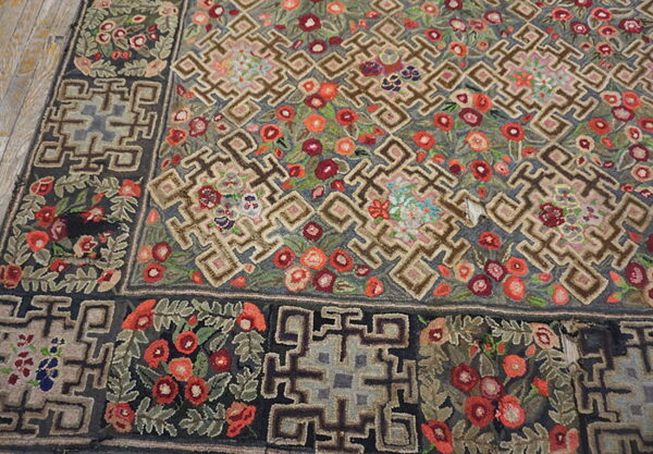 Textured rug with interlocking gray and brown geometric patterns and dense red flowers on distressed wood flooring.