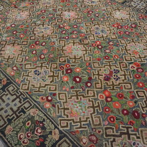 Textured rug displaying dense red and pink florals woven between interlocking brown geometric shapes on wood floors.