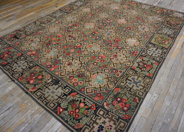 Muted green and khaki rug with red florals and geometric borders lying on distressed gray wood planks.