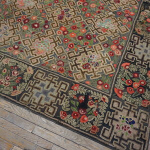 Rustic looped rug with geometric fretwork and dense red floral patterns on distressed wood planks.