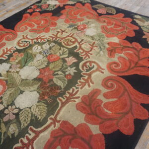 A densely hooked rug featuring red scrolling leaves, multicolored florals, and a dark black border on wood flooring.
