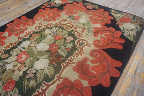 A densely hooked rug featuring red scrolling leaves, multicolored florals, and a dark black border on wood flooring.