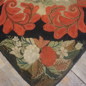 Black ground rug with looped red scrolled vines and detailed floral border on distressed wood plank floor.