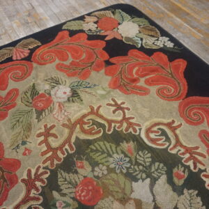 Textured rug featuring red acanthus leaf scrolls, dark borders, and a tan field on distressed gray flooring.