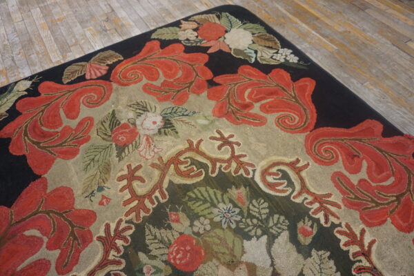 Textured rug featuring red acanthus leaf scrolls, dark borders, and a tan field on distressed gray flooring.