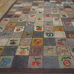 Checkerboard rug with folk flowers and concentric squares in muted grays and browns on wood planks.