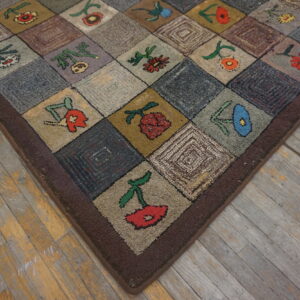 Rustic hooked rug with multicolored floral patchwork squares displayed on worn gray and yellow hardwood flooring.