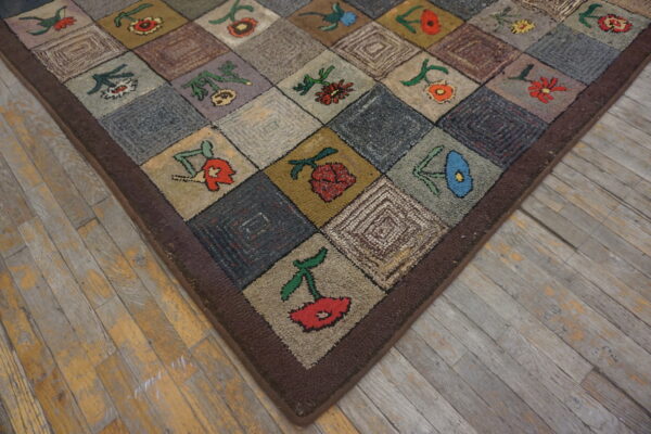 Rustic hooked rug with multicolored floral patchwork squares displayed on worn gray and yellow hardwood flooring.