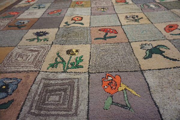 A textured rug features a patchwork grid of squares containing colorful flowers and geometric designs.