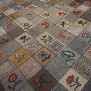 A textured rug featuring a colorful floral patchwork pattern on muted gray and brown squares.