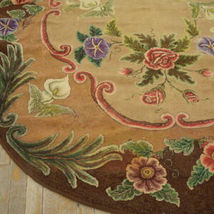 Tawny round rug featuring textured red, purple, and white botanical patterns, lying on distressed wood flooring.