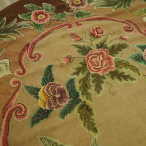 Round tan rug with detailed pink and green floral pattern rests on light rustic wood flooring.