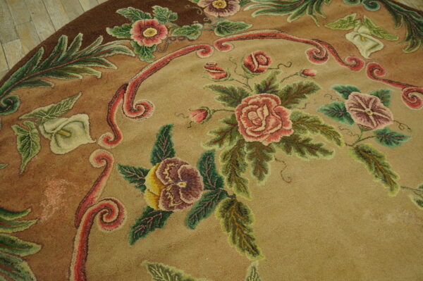 Round tan rug with detailed pink and green floral pattern rests on light rustic wood flooring.