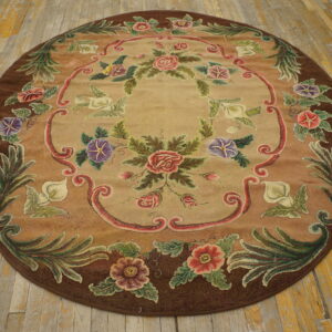 Round floral rug in tan, brown, pink, and green colors displayed on worn light hardwood plank flooring.