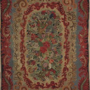 Textured, multicolored rug with a dense floral center and wide, heavily scrolled red and blue ornamental borders.