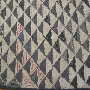 A textured hooked rug featuring a diamond pattern of alternating gray and beige blocks on wood flooring.