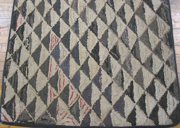 A textured hooked rug featuring a diamond pattern of alternating gray and beige blocks on wood flooring.