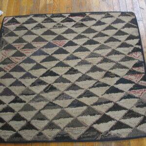 Textured square rug featuring dark grey and off-white triangles, with small red accents, lying on a wood floor.