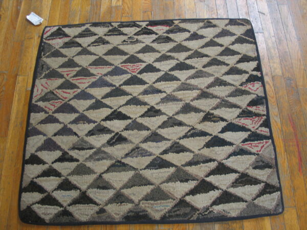 Textured square rug featuring dark grey and off-white triangles, with small red accents, lying on a wood floor.