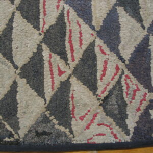 Textured black and beige rug with a diamond pattern, accented by bright red stripes, resting on wood floor.