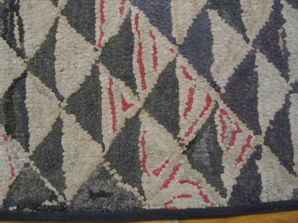 Textured black and beige rug with a diamond pattern, accented by bright red stripes, resting on wood floor.