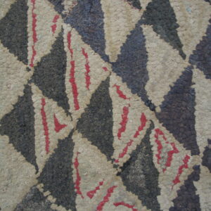 Close-up of a bumpy, rustic rug with large triangles in charcoal, beige, and sparse red accents.