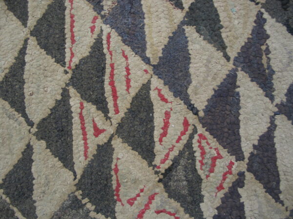 Close-up of a bumpy, rustic rug with large triangles in charcoal, beige, and sparse red accents.