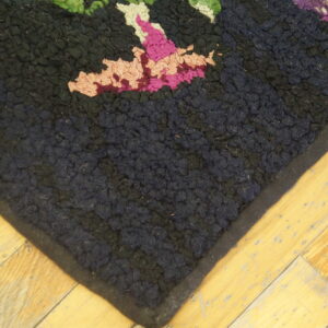 Thick pile rug with dark navy and black background features bright pink and green floral accents on wood flooring.
