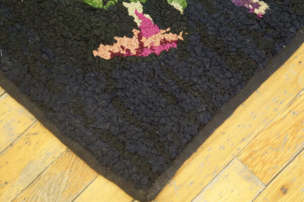 Thick pile rug with dark navy and black background features bright pink and green floral accents on wood flooring.