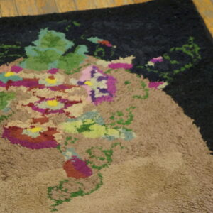A dark shaggy rug with a tan and multicolored abstract floral bouquet rests on distressed wood flooring.