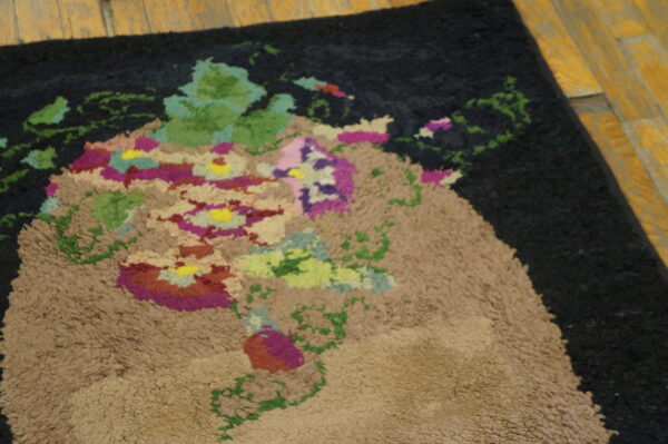 A dark shaggy rug with a tan and multicolored abstract floral bouquet rests on distressed wood flooring.