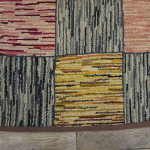 A heavily textured block rug in pink, yellow, and blue-gray colors rests on light wood planks.