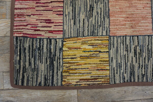 A heavily textured block rug in pink, yellow, and blue-gray colors rests on light wood planks.