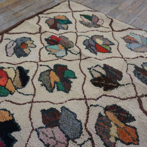 Cream-colored textured rug with a dark brown grid holding brightly colored, stylized leaf motifs on wood floor.