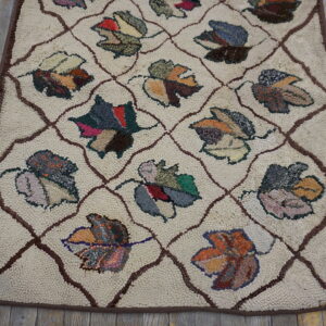 Cream textured rug with a brown lattice and multicolored leaf pattern resting on distressed wood flooring.