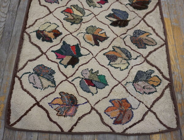 Cream textured rug with a brown lattice and multicolored leaf pattern resting on distressed wood flooring.