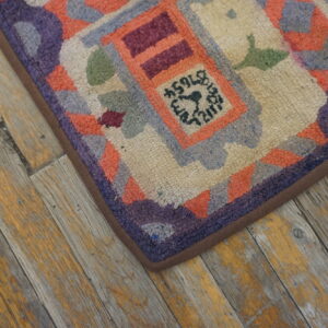 A colorful looped pile rug with geometric patterns in purple, orange, green, and cream rests on distressed wood flooring.