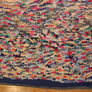 Highly textured multi-color rag rug in red, blue, green, and beige with a navy border on wood flooring.
