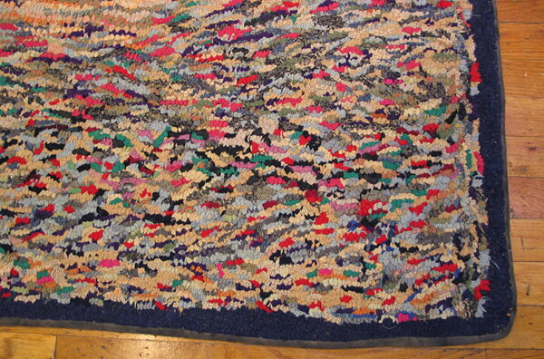 Highly textured multi-color rag rug in red, blue, green, and beige with a navy border on wood flooring.