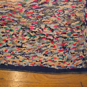 Multicolored shaggy rug featuring red, beige, green, and blue patches, with a navy border on wood planks.