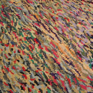 Multicolored rug with chunky, diagonal texture showing shades of red, blue, green, purple, and tan.