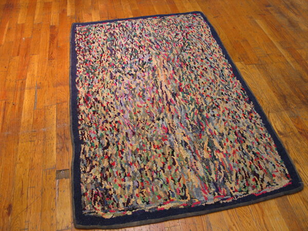 Multicolor shaggy rug with an abstract pattern and dark navy border is placed on a shiny wood plank floor.