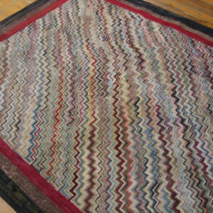 Zigzag patterned rug in various colors, framed by red and black borders, placed on wood flooring.