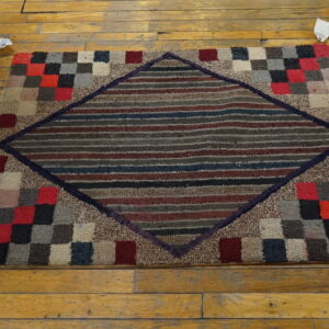 Textured multicolored rug displaying a striped central diamond framed by a checkered block border on wood flooring.