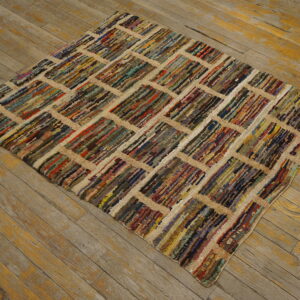 Shaggy, multicolored rug with a geometric tan grid pattern lying on distressed wooden floorboards.