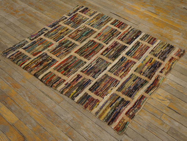 Shaggy, multicolored rug with a geometric tan grid pattern lying on distressed wooden floorboards.