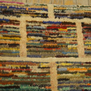 Textured high-pile rug with a cream grid pattern separating blocks of multicolored horizontal stripes on wood.