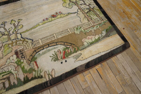 Hooked rug with a pastoral scene of a bridge and trees in muted greens and browns on rustic wood flooring.